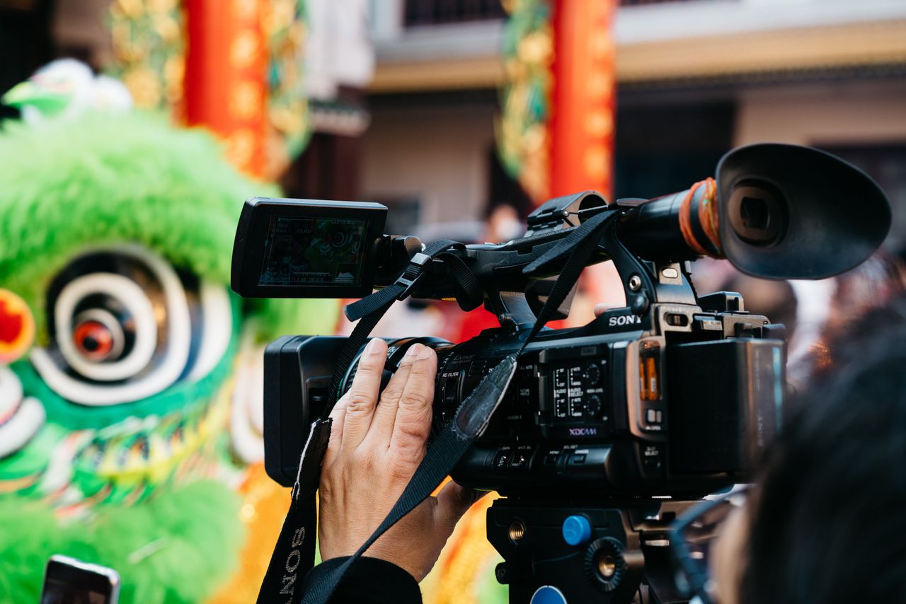 Menu Close-up of a videographer filming a colorful Chinese lion dance celebration outdoors.