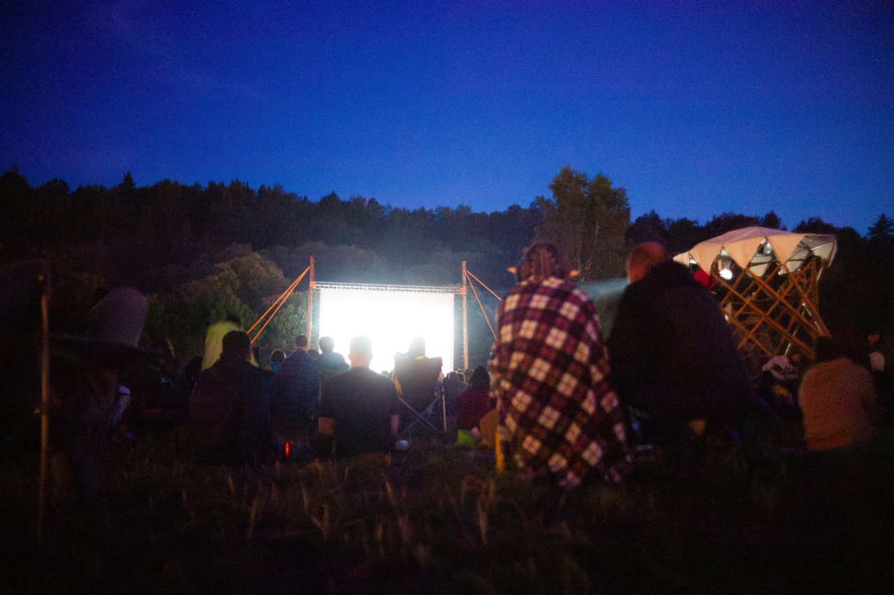 Menu Adults gather outdoors for a night movie screening under the stars.
