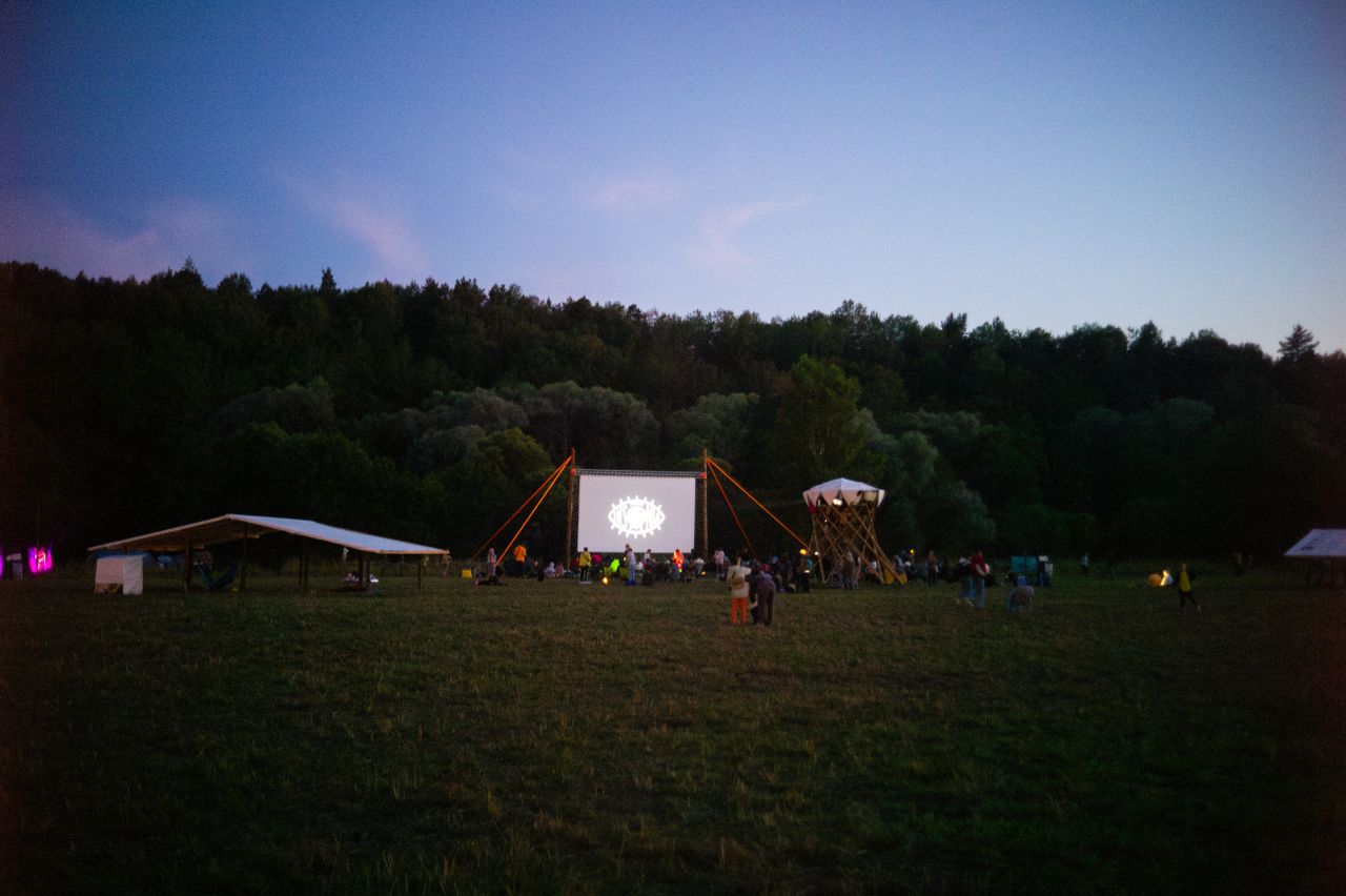 Menu A twilight outdoor movie event in a meadow with people gathered around a screen.