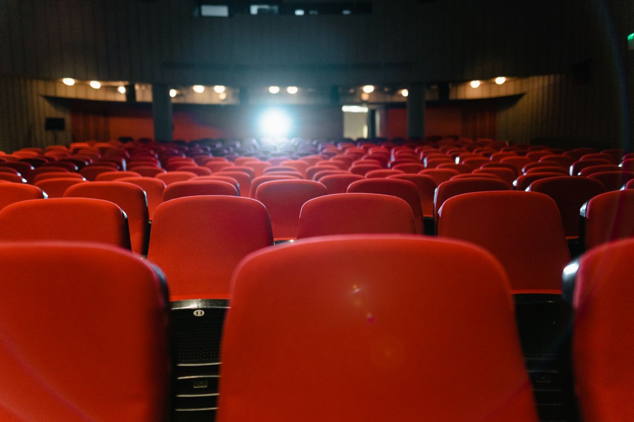 Menu A view of an empty cinema with rows of red seats facing the illuminated screen.